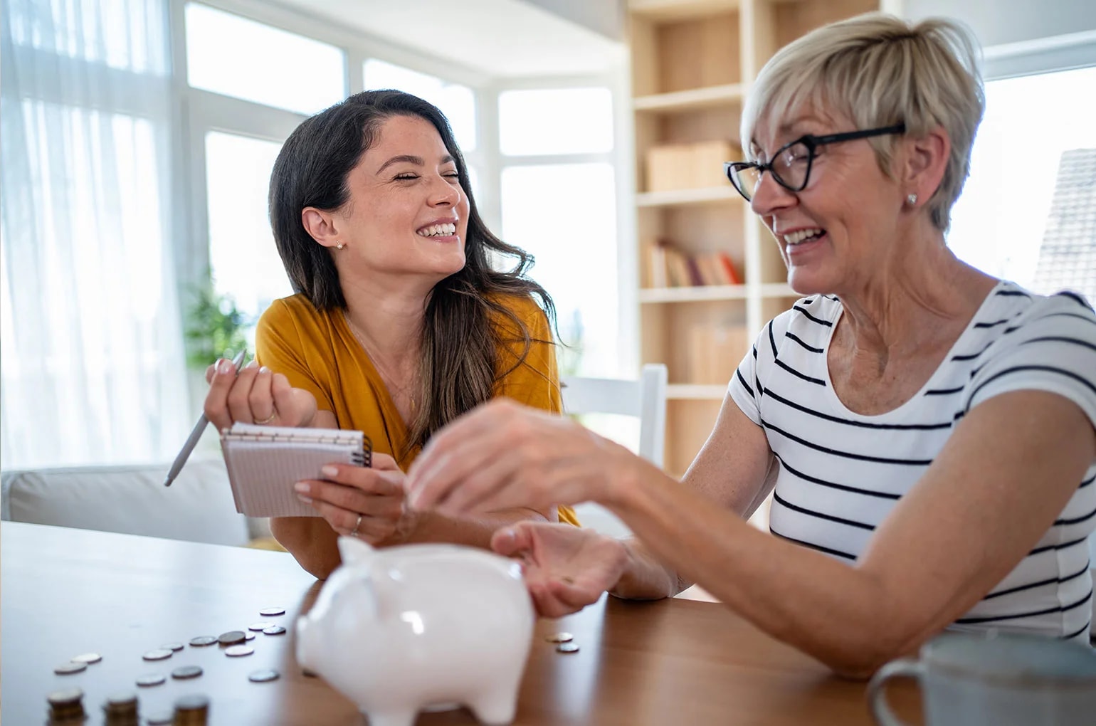 Zwei Personen sitzen am Tisch und planen gemeinsam Finanzen mit Notizblock, Münzen und Sparschwein – Symbolbild für langfristige Planung und Altersvorsorge für Selbständige.