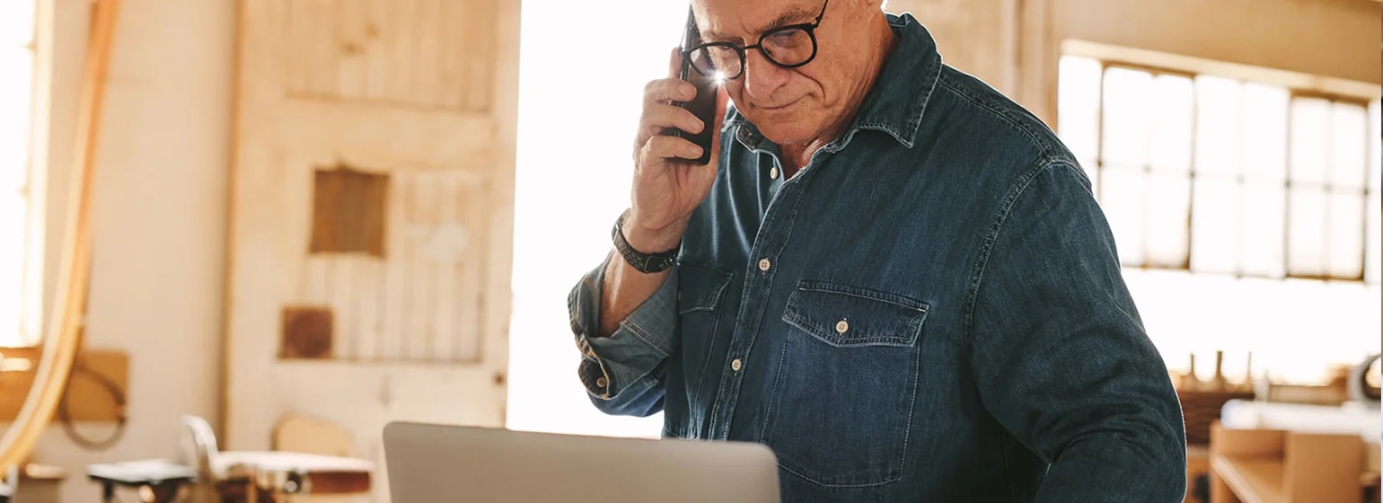 Person arbeitet in einer Werkstatt mit Laptop und Smartphone zwischen Maschinen und Werkzeugen – Symbolbild für Digitalisierung im Mittelstand und den Einsatz digitaler Technologien im Arbeitsalltag.