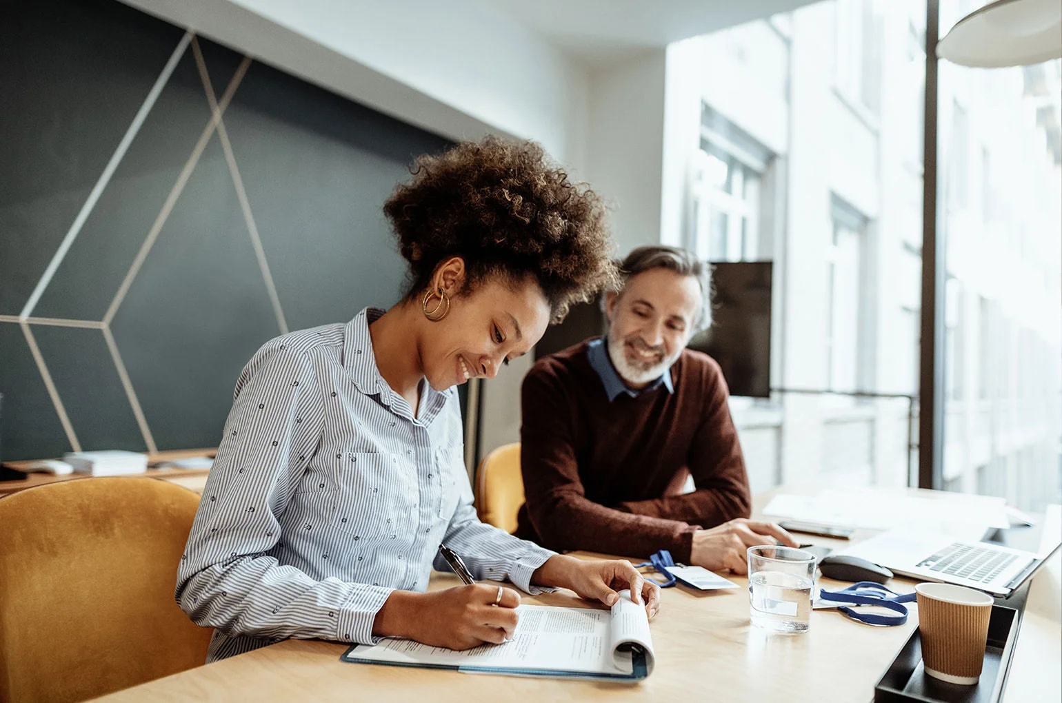Zwei Personen sitzen an einem Tisch und prüfen gemeinsam Vertragsunterlagen im Büro – Symbolbild für die Ausarbeitung und Unterzeichnung eines Freelancer Vertrag.
