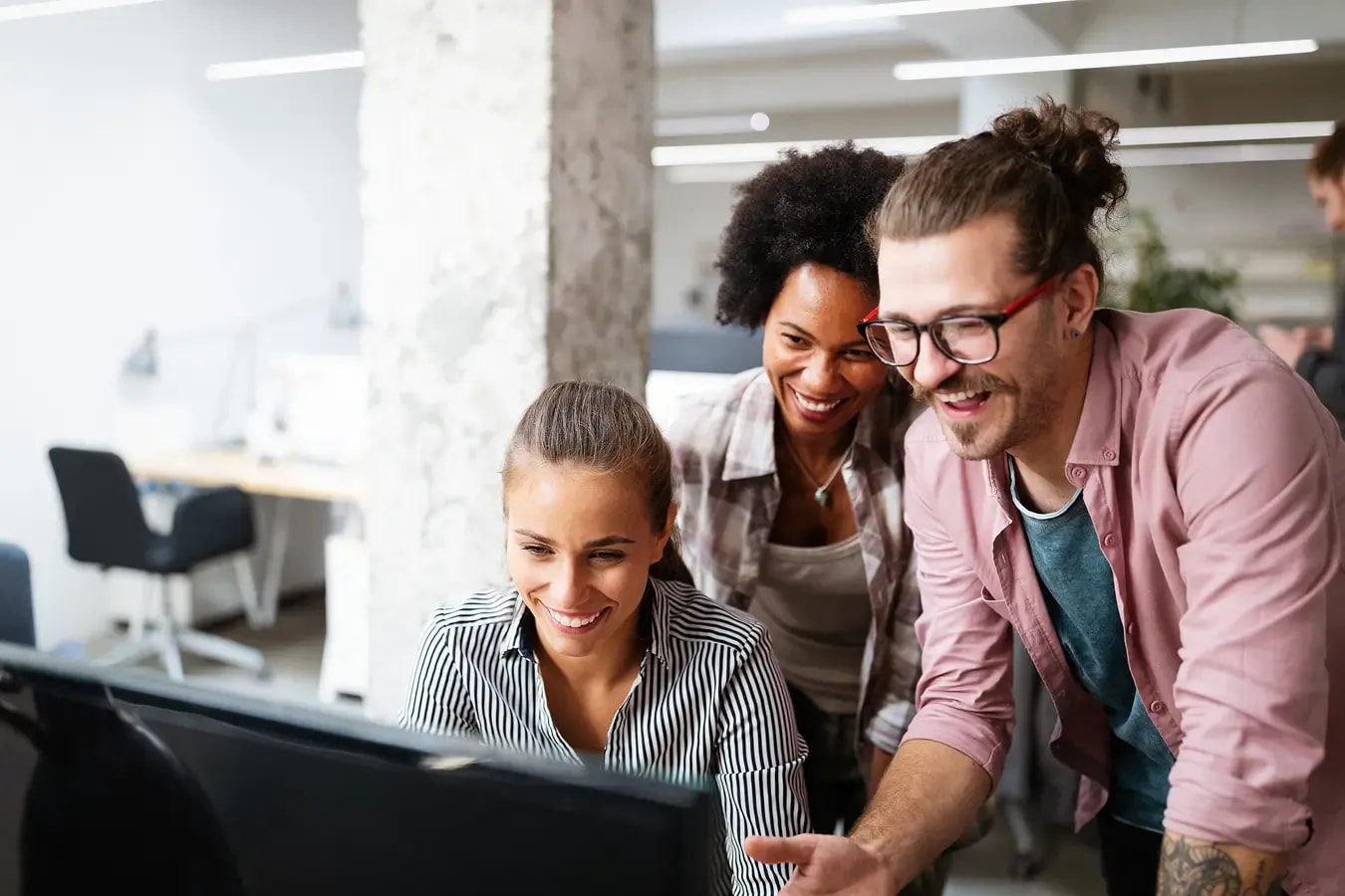 3 IT-Freelancer schauen auf einen Bildschirm und lachen.