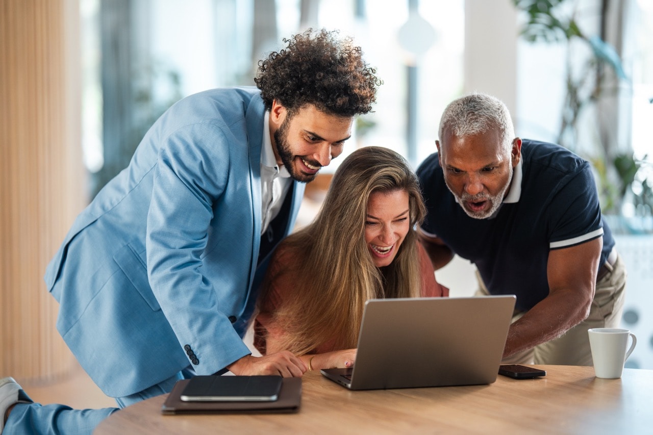 Drei Personen schauen begeistert gemeinsam auf einen Laptop, vermutlich bei der Durchsicht eines Projekts oder Profils auf einem Freelancer-IT-Portal.
