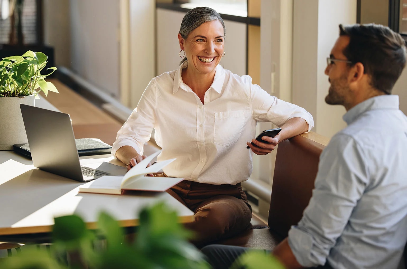 Zwei Personen besprechen Unterlagen an einem Tisch mit Laptop und Smartphone in einer Büroumgebung – Symbolbild für rechtliche Abstimmungen und die Prüfung von Scheinselbständigkeit Kriterien in Projekten.