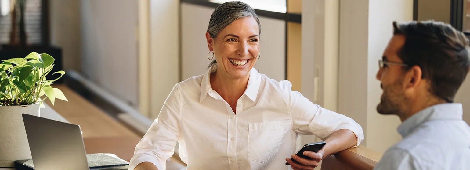 Zwei Personen besprechen Unterlagen an einem Tisch mit Laptop und Smartphone in einer Büroumgebung – Symbolbild für rechtliche Abstimmungen und die Prüfung von Scheinselbständigkeit Kriterien in Projekten.