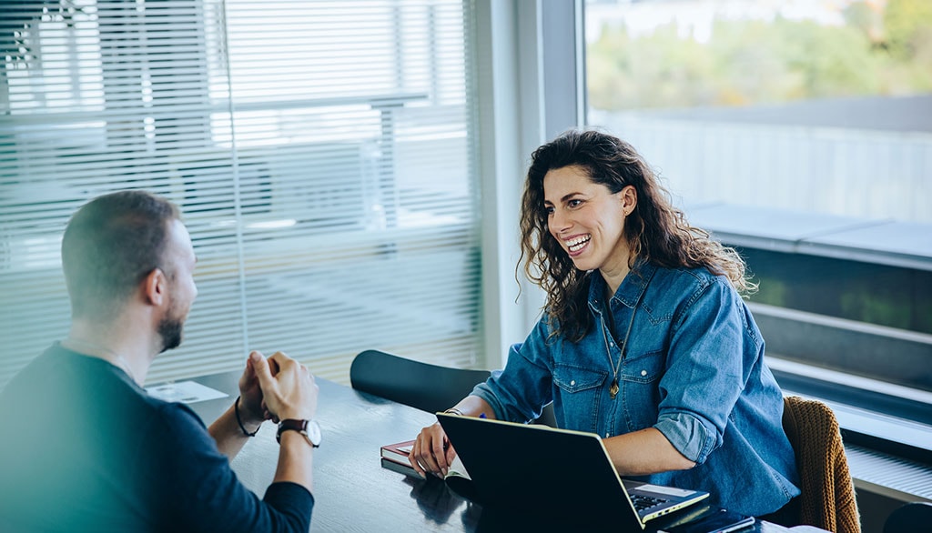 Austausch zwischen Projektbeteiligten in einem Büro, Frau mit Laptop im Gespräch mit einem Kollegen.