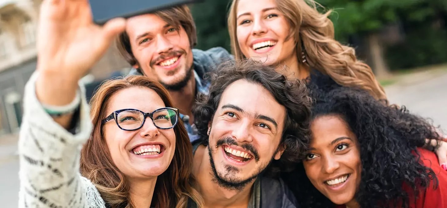 Gruppe von fünf Personen nimmt gemeinsam ein Selfie im Freien auf, aufgenommen aus kurzer Distanz mit einem Smartphone.