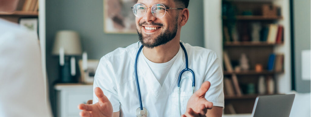Arzt mit Stethoskop sitzt an Tisch und lächelt