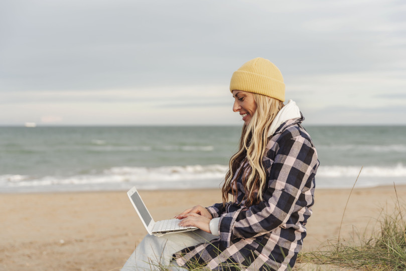 Frau sitzt mit Laptop arbeitend am Strand